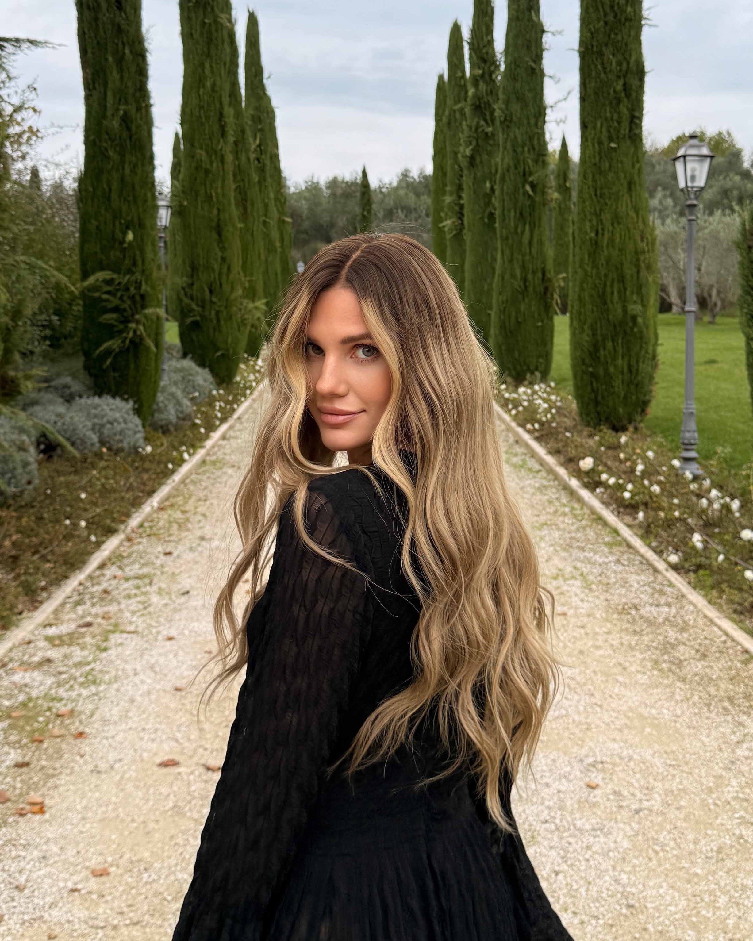 Woman wearing a long BHBD wig with dark blonde roots that transitions into slightly lighter lengths.